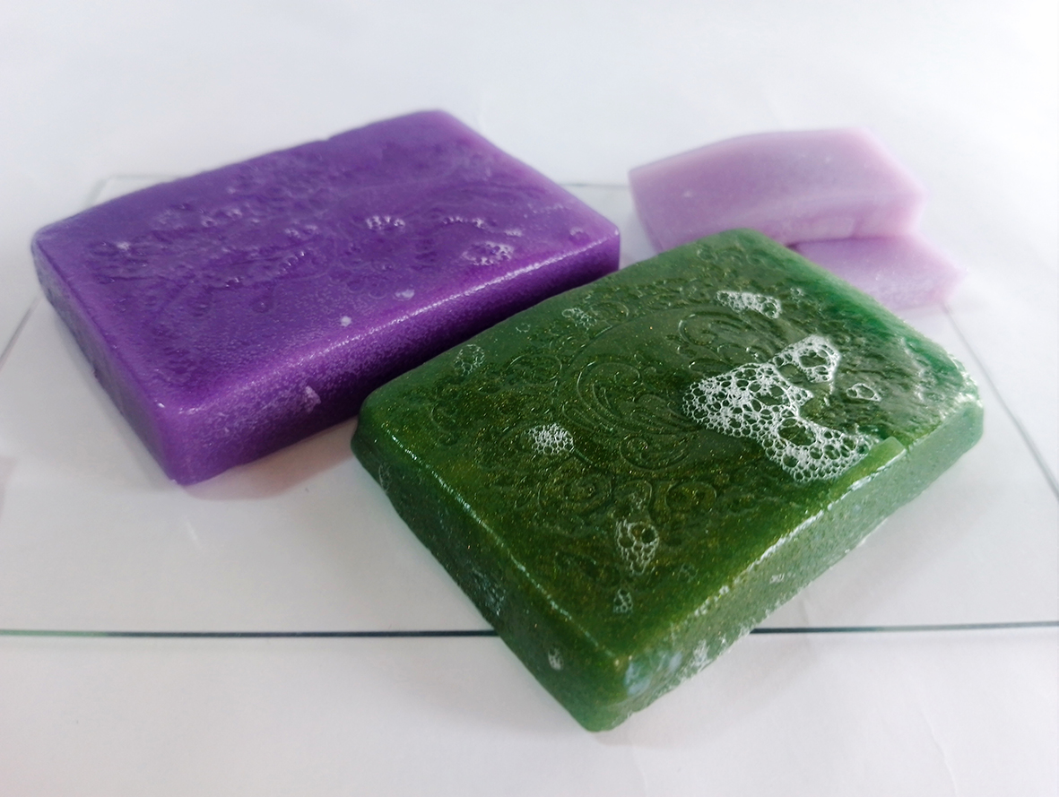 Primer plano de jabón de gelatina espumado en color verde y morado colocado sobre un fondo blanco.